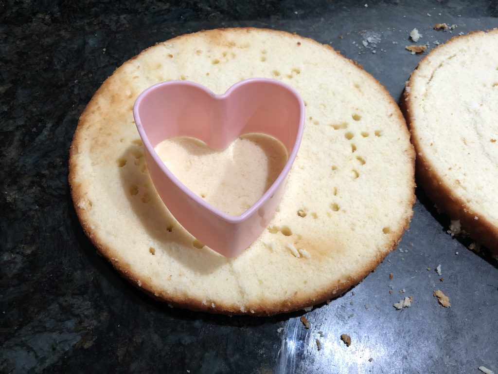 using a cookie cutter to cut out heart shaped cakes 